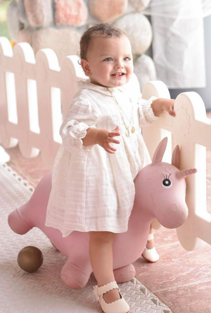 Toddler girl in white dress on pink unicorn bounce toy.
