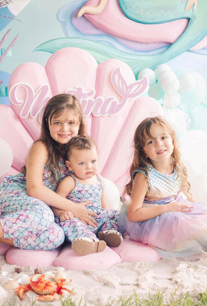 Martina's mermaid-themed birthday: Three girls in mermaid outfits on a seashell seat.